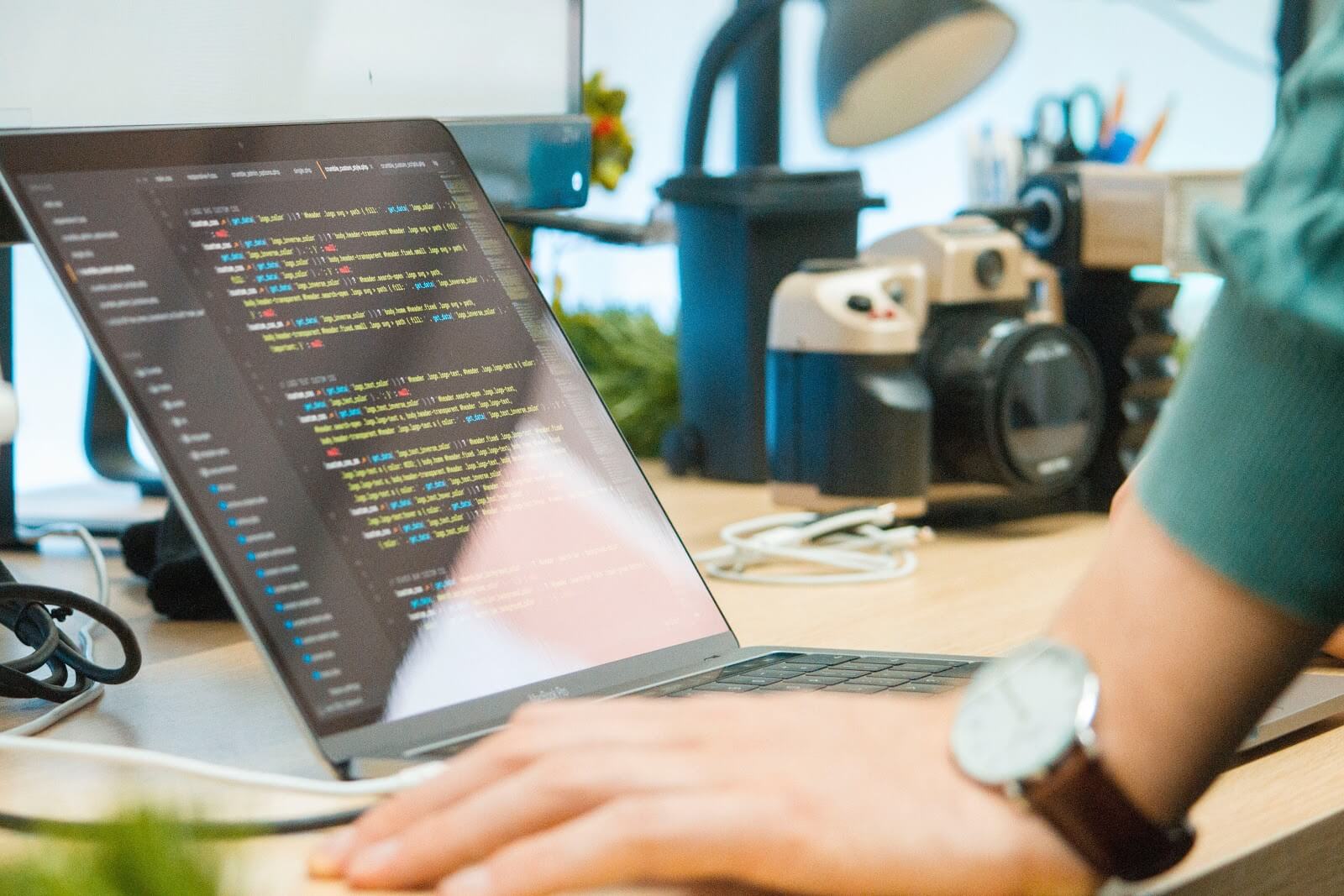 Cómo convertirse en un desarrollador de software: una mano se apoya en un escritorio frente a la pantalla de una computadora portátil cubierta de código