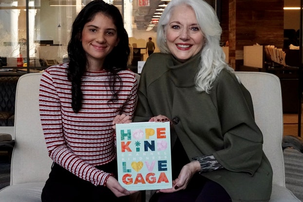   Cynthia Germanotta (derecha), presidenta y cofundadora, y Aysha Mahmood, editora, ambas de la Fundación Born This Way, sentadas sosteniendo un libro.